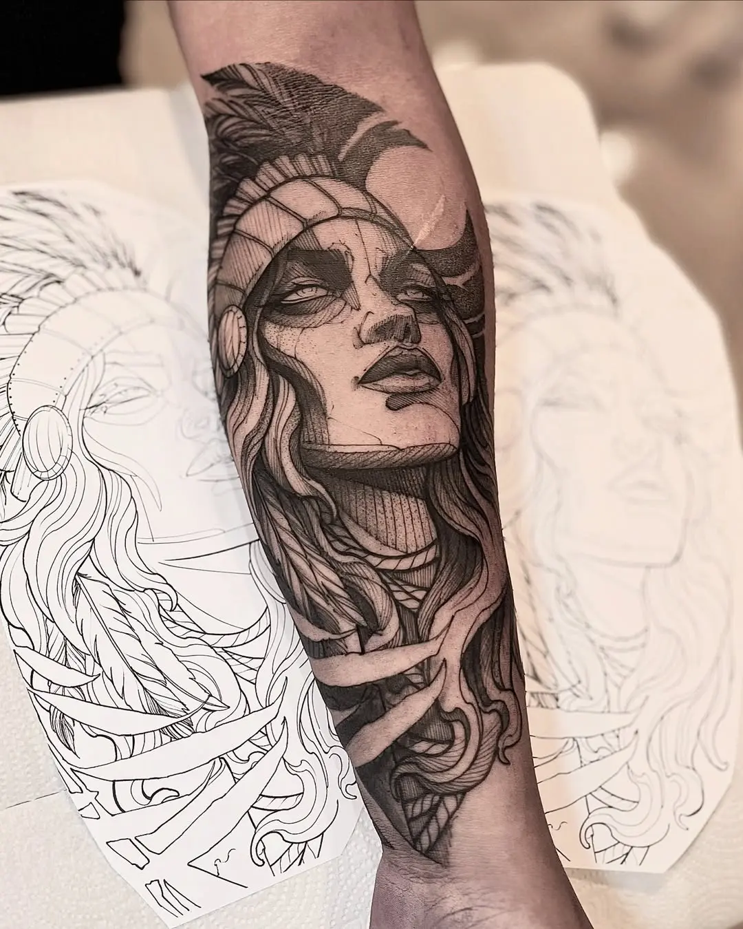 Tatuagem blackwork de guerreira indígena com cocar e tranças no antebraço