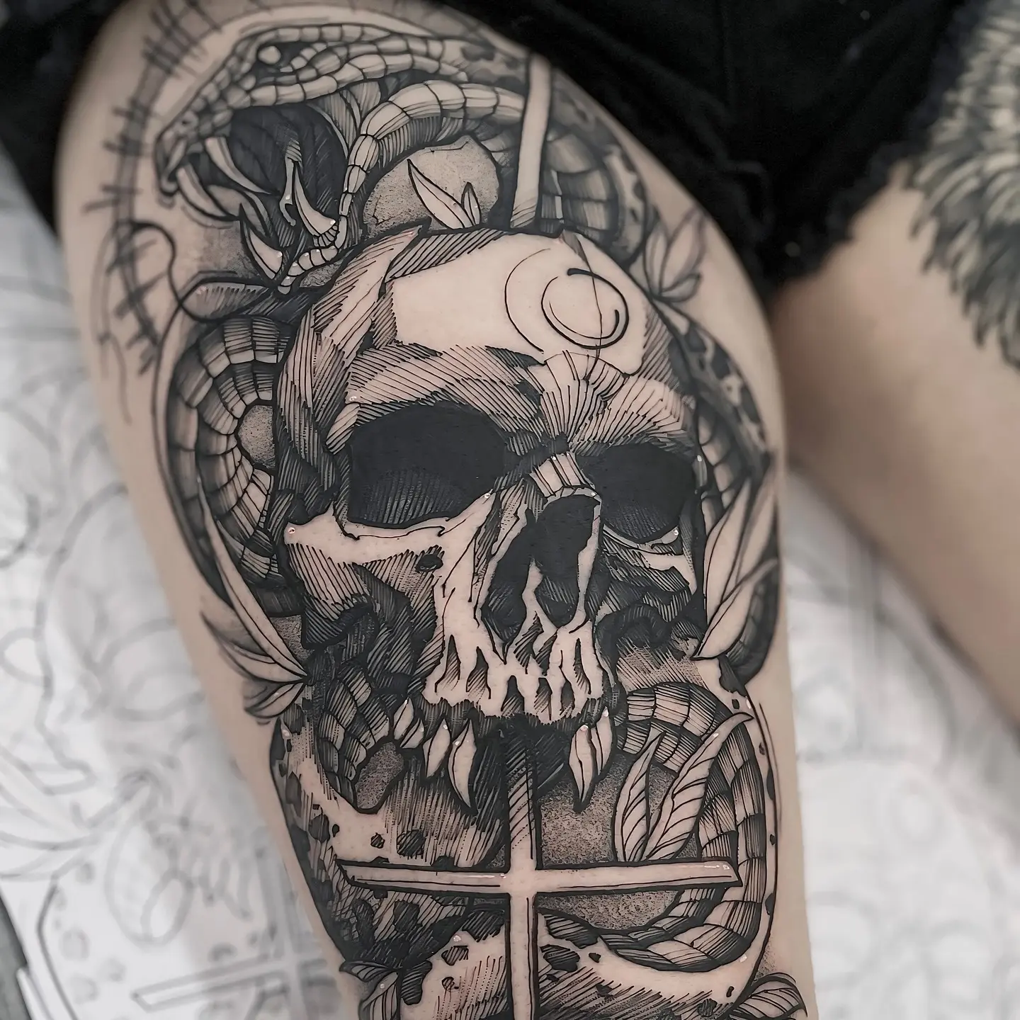 Tatuagem blackwork de caveira com cobra e cruz na coxa
