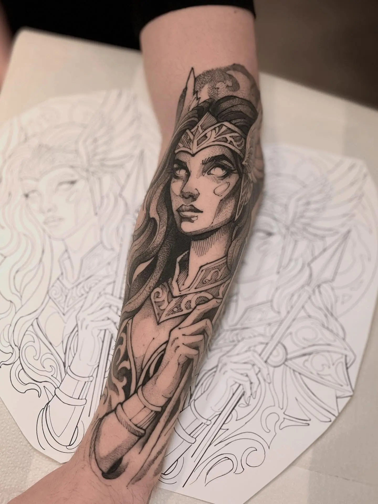 Tatuagem blackwork de guerreira com armadura e coroa no antebraço